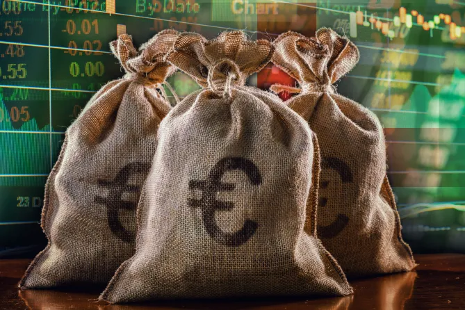 :“Euro banknotes in bags in front of a chart displaying trade numbers, symbolizing financial analysis and currency markets”.