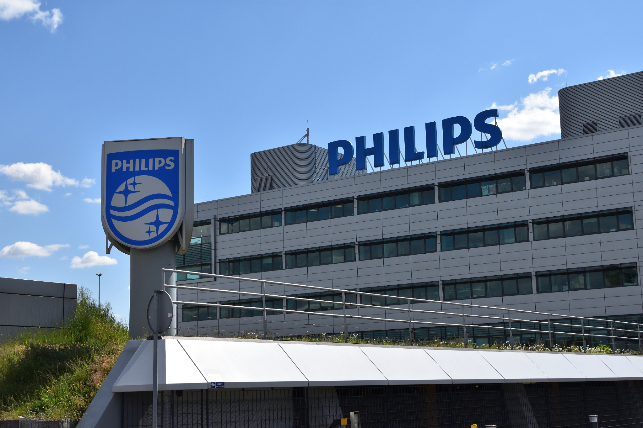 Modern building with large blue "PHILIPS" signage and logo on a signpost, under a clear blue sky with a few clouds.