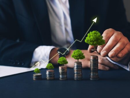 Businessman holding coin with graph and tree growing on money stack