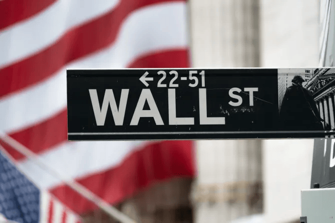 :"Wall Street sign at the New York Stock Exchange with American flag in background on a bright, sunny summer day".