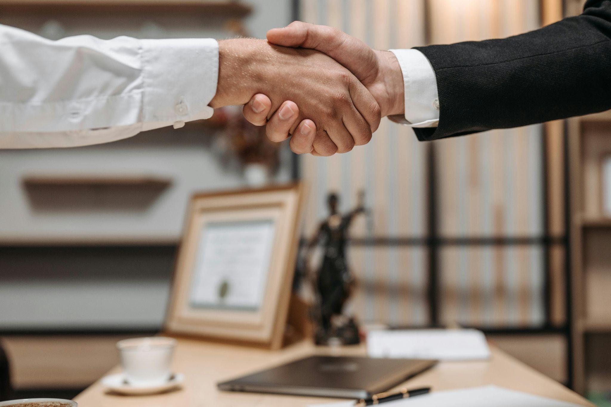 "Close-up of a confident handshake between two business professionals in a modern office setting, symbolizing a partnership.”