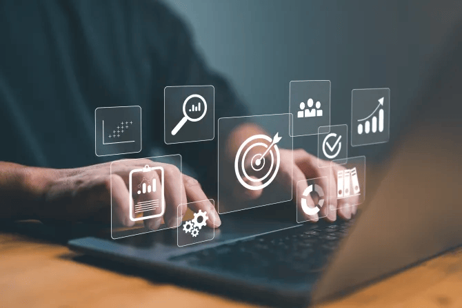 :”Hands typing on a laptop with overlay icons representing strategies such as targeting, data analysis, graphs, and marketing”.