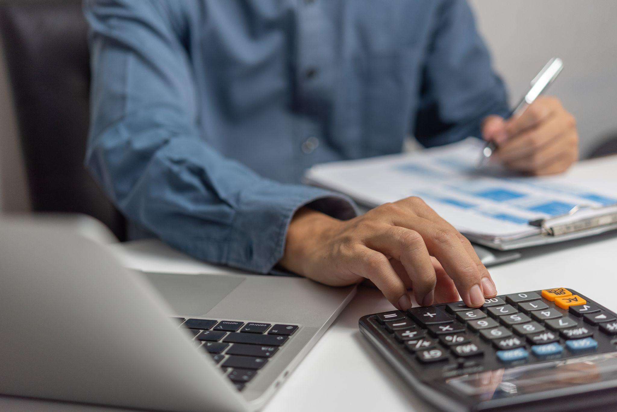 Businessman using calculator and accounting documents at desk with laptop computer.