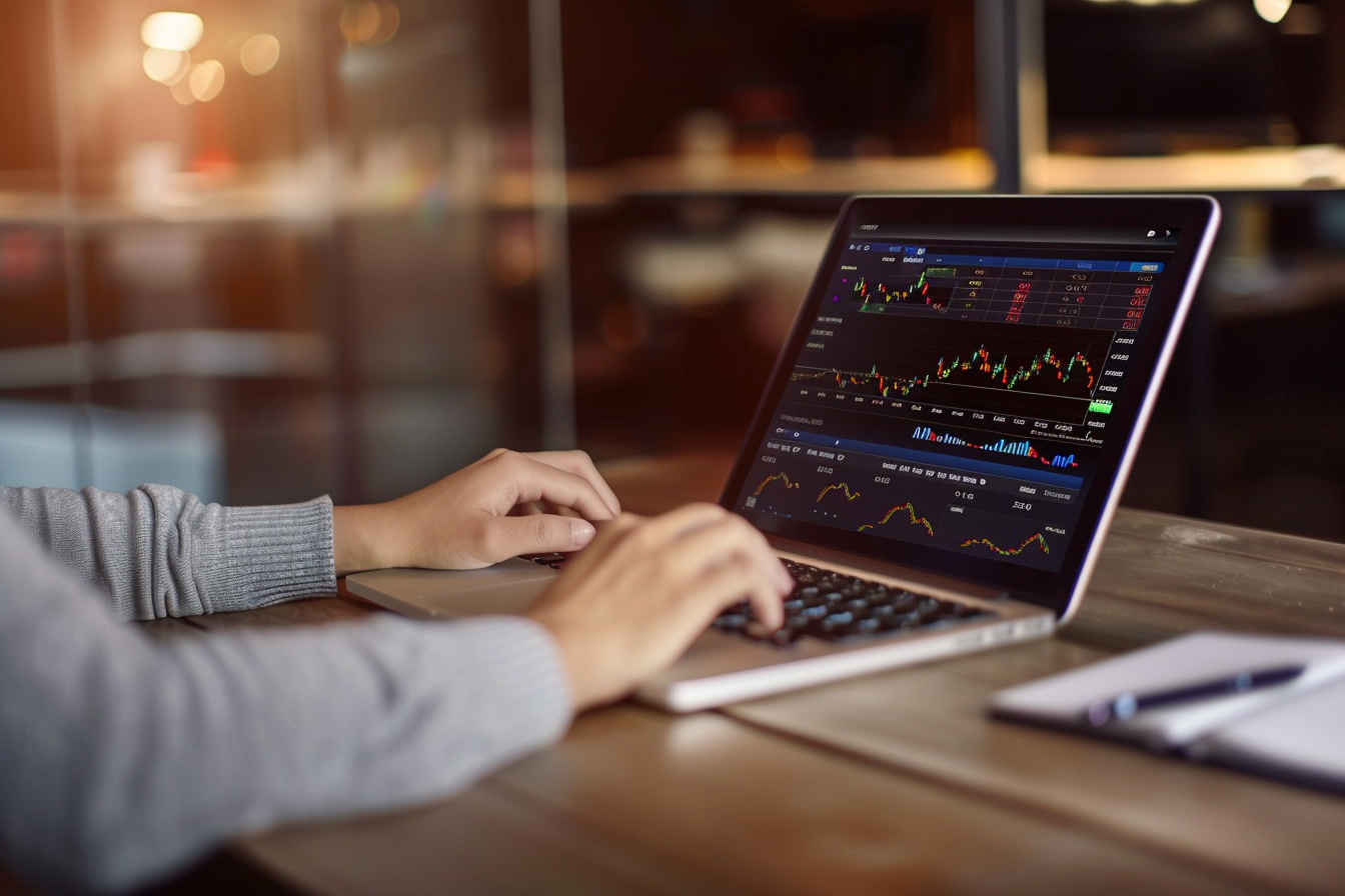 Home office setup with a laptop displaying a trading platform. Blurred background, focused user, notebook and pen.