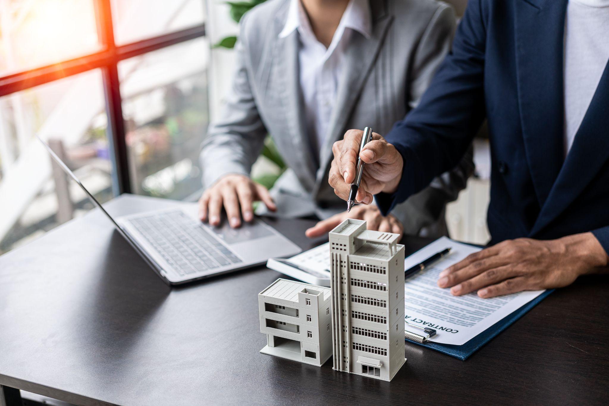 Agents offer housing contracts. Businessman holds small house model with property insurance at home sales office table.