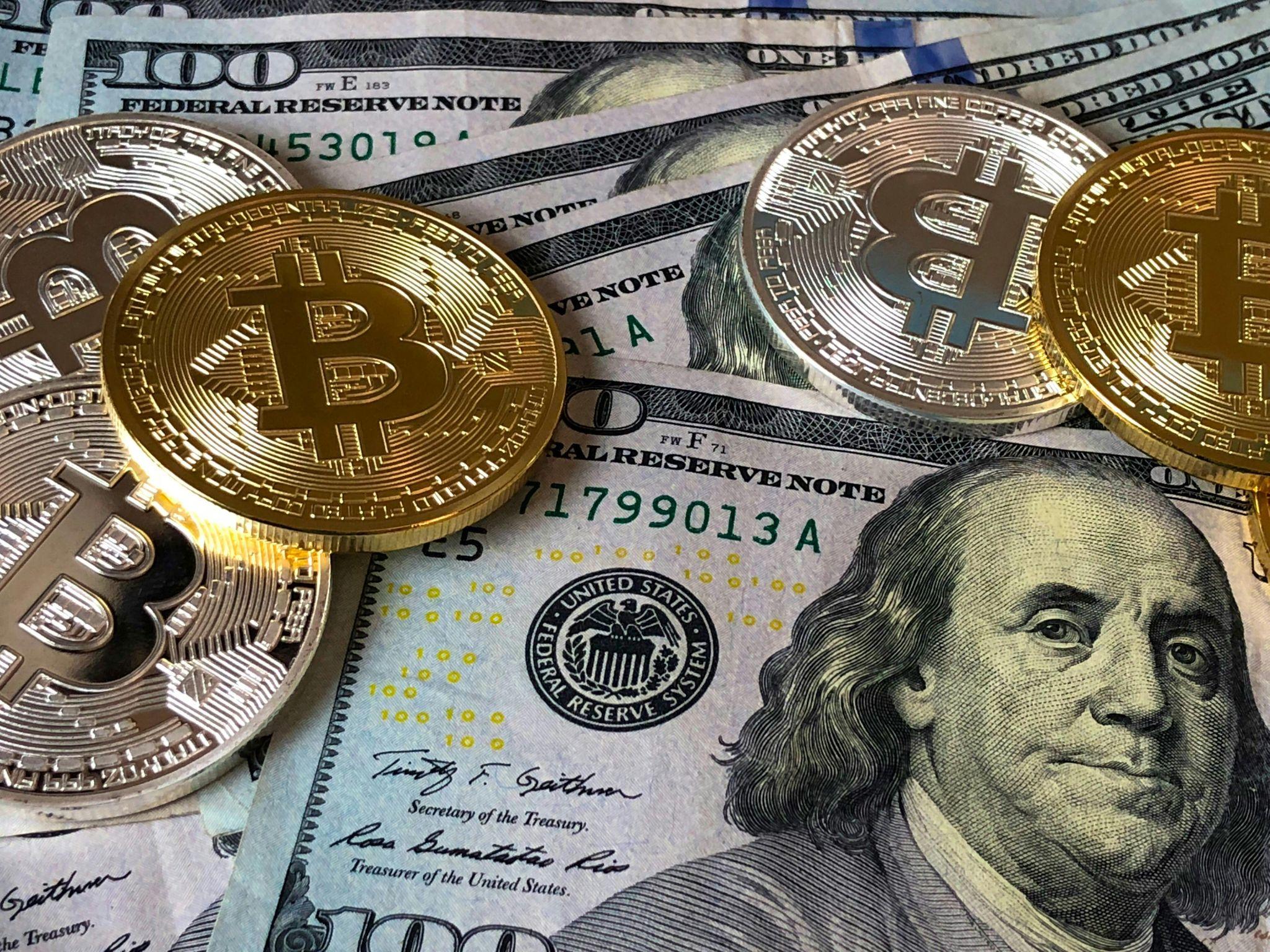 "Close-up of Bitcoin coins placed on top of multiple U.S. hundred-dollar bills, highlighting cryptocurrency and cash."